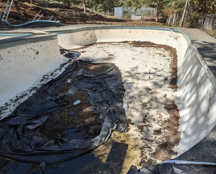 A pool filled with dirt and debris on top of the ground.